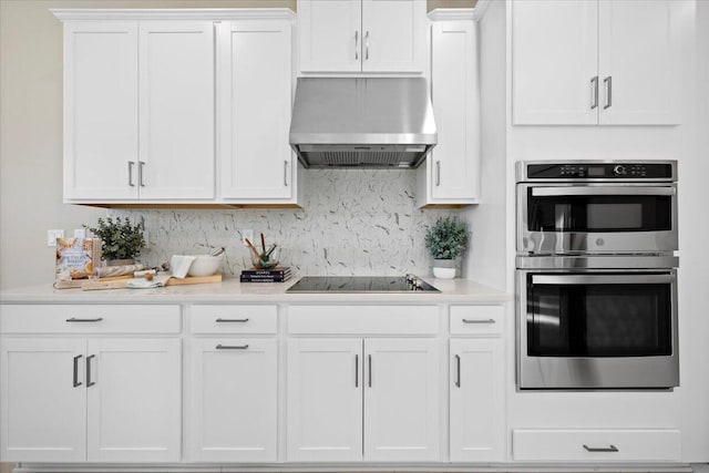 kitchen with black electric stovetop, stainless steel double oven, white cabinetry, and wall chimney range hood