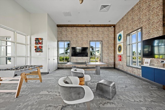 living room featuring a healthy amount of sunlight, carpet floors, brick wall, and a towering ceiling