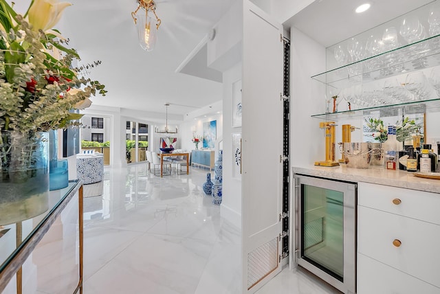 bar with white cabinetry, hanging light fixtures, and beverage cooler