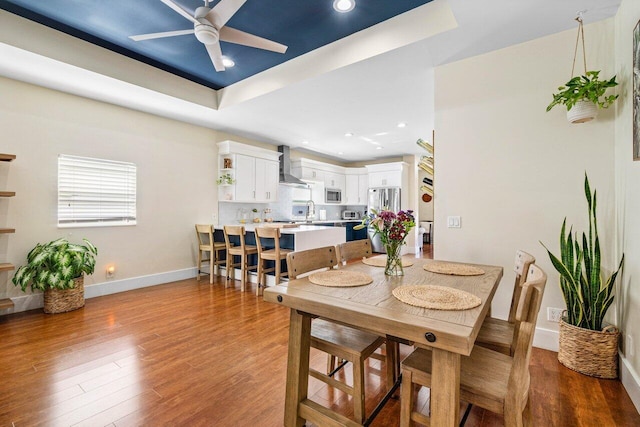 dining room with dark hardwood / wood-style floors, ceiling fan, a tray ceiling, and sink