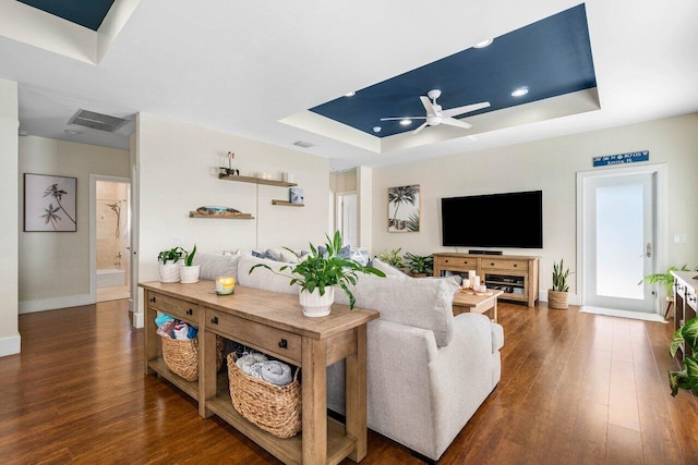 living room with a tray ceiling, ceiling fan, and dark hardwood / wood-style floors