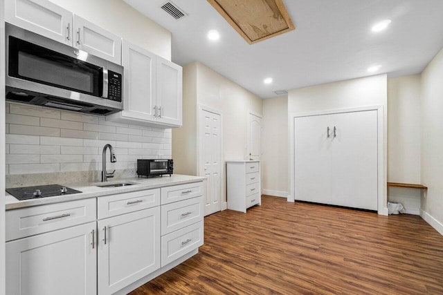 kitchen featuring light countertops, stainless steel microwave, a sink, and white cabinetry