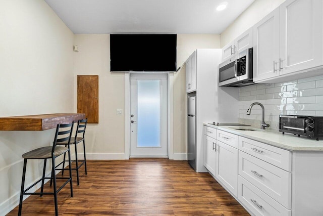 kitchen with sink, dark wood-type flooring, stainless steel appliances, backsplash, and white cabinets