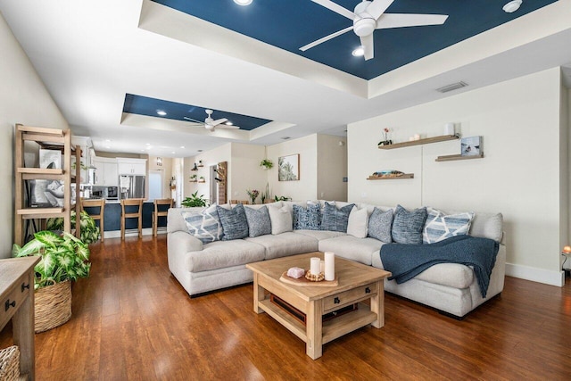 living room with dark wood-type flooring, ceiling fan, and a tray ceiling