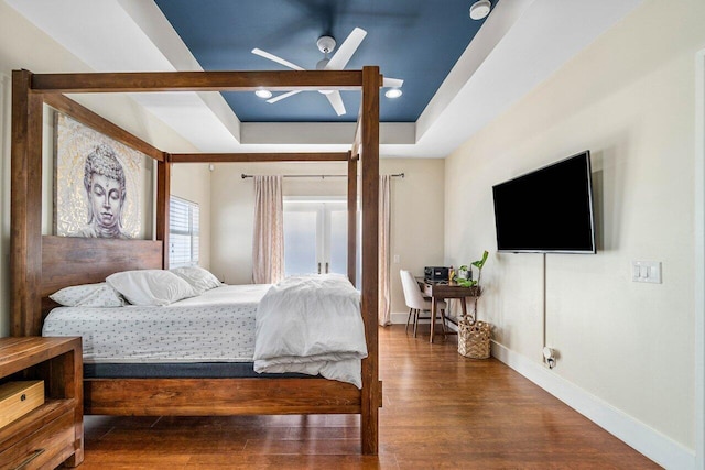 bedroom with a raised ceiling, ceiling fan, and dark hardwood / wood-style flooring