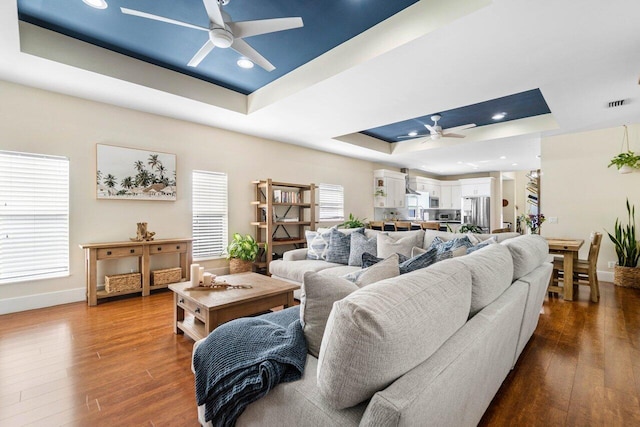 living area featuring ceiling fan, a tray ceiling, wood finished floors, and visible vents