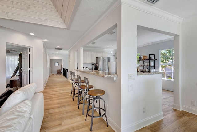 kitchen with a kitchen breakfast bar, light hardwood / wood-style flooring, light stone countertops, white cabinetry, and stainless steel refrigerator