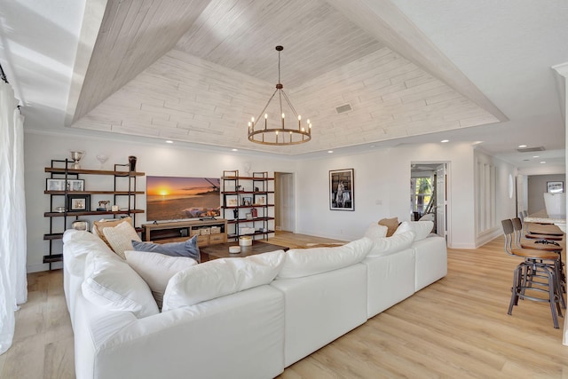 living room featuring an inviting chandelier, a raised ceiling, ornamental molding, and light hardwood / wood-style flooring