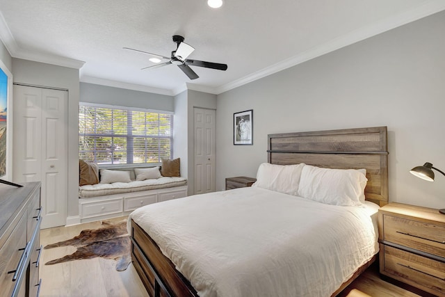 bedroom with multiple closets, light hardwood / wood-style floors, ceiling fan, and ornamental molding