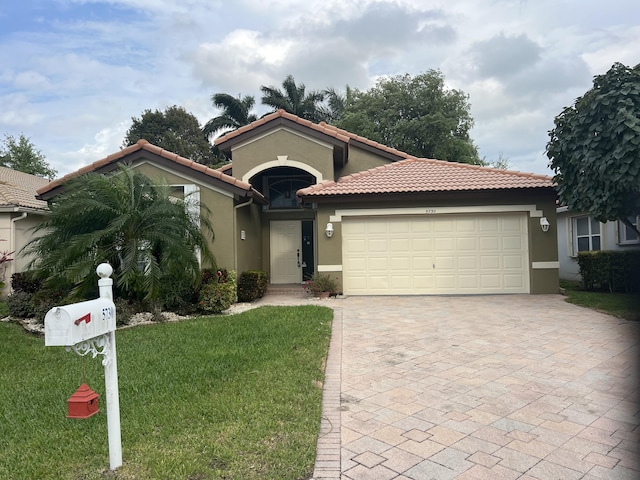 mediterranean / spanish-style house featuring stucco siding, a front lawn, a garage, a tiled roof, and decorative driveway