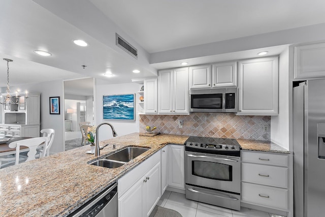 kitchen featuring kitchen peninsula, light stone counters, stainless steel appliances, sink, and white cabinetry