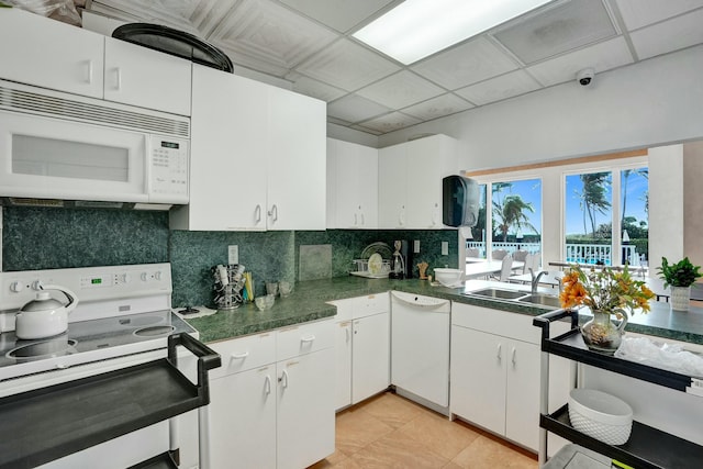 kitchen with a drop ceiling, white appliances, sink, light tile patterned floors, and white cabinetry