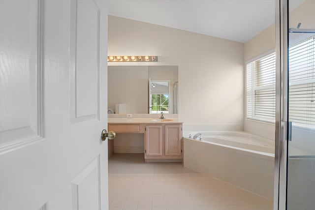 bathroom with tile patterned floors, a relaxing tiled tub, a healthy amount of sunlight, and vanity