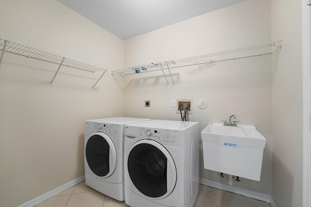 clothes washing area featuring washing machine and clothes dryer, sink, light tile patterned flooring, and a textured ceiling