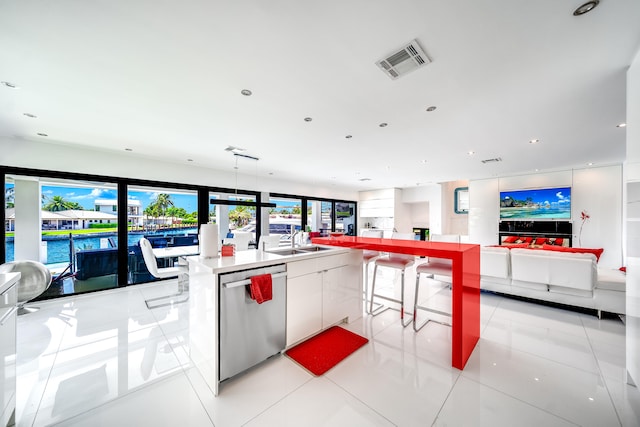 kitchen with light tile patterned floors, white cabinets, stainless steel dishwasher, a center island with sink, and a water view