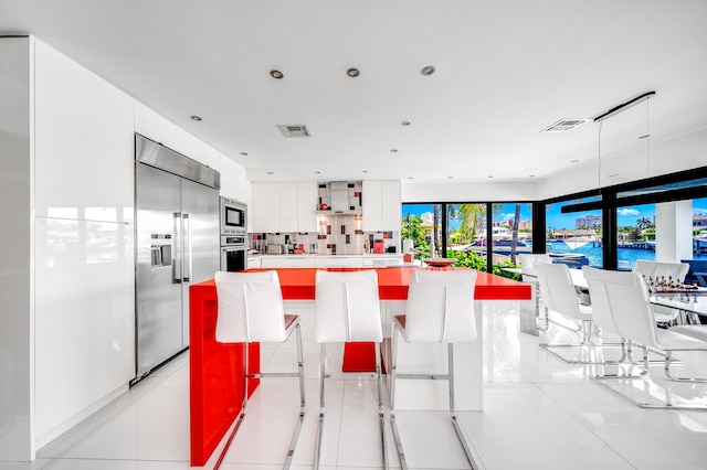 kitchen with a kitchen bar, a kitchen island, built in appliances, a water view, and white cabinetry