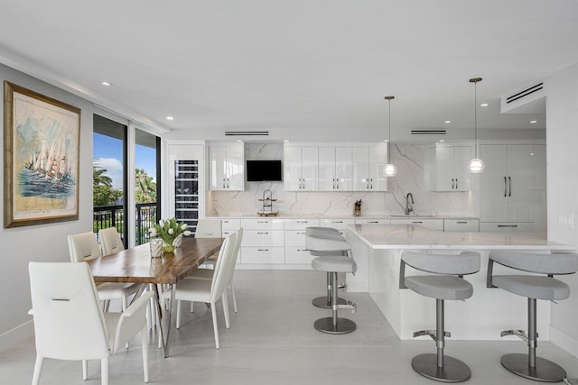 kitchen with a breakfast bar, backsplash, white cabinets, sink, and decorative light fixtures