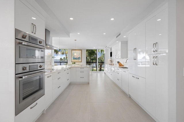 kitchen with wall chimney range hood, sink, hanging light fixtures, tasteful backsplash, and white cabinetry