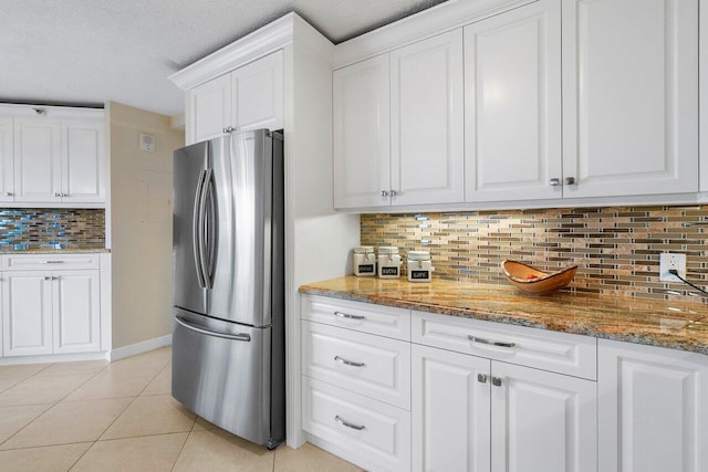 kitchen featuring decorative backsplash, stone countertops, white cabinets, stainless steel refrigerator, and light tile patterned flooring