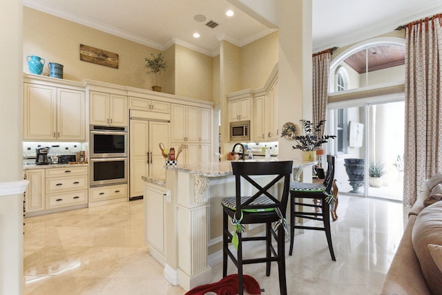 kitchen with a kitchen bar, built in appliances, cream cabinets, and a towering ceiling