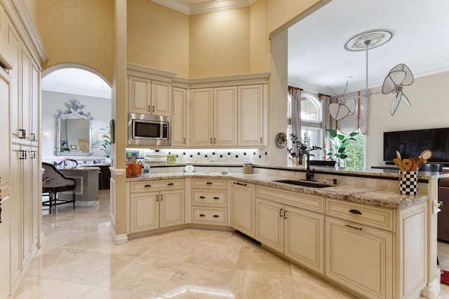 kitchen featuring light stone countertops, sink, stainless steel microwave, crown molding, and cream cabinetry