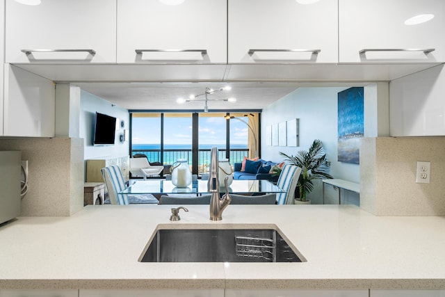 kitchen with light stone countertops, sink, white cabinets, and a wall of windows