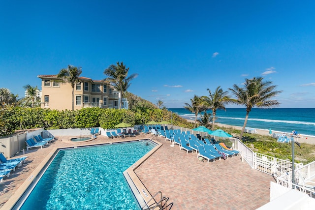 view of pool with a water view, a view of the beach, and a patio