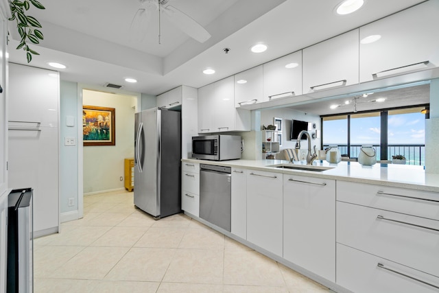 kitchen with sink, light tile patterned floors, appliances with stainless steel finishes, a raised ceiling, and white cabinets