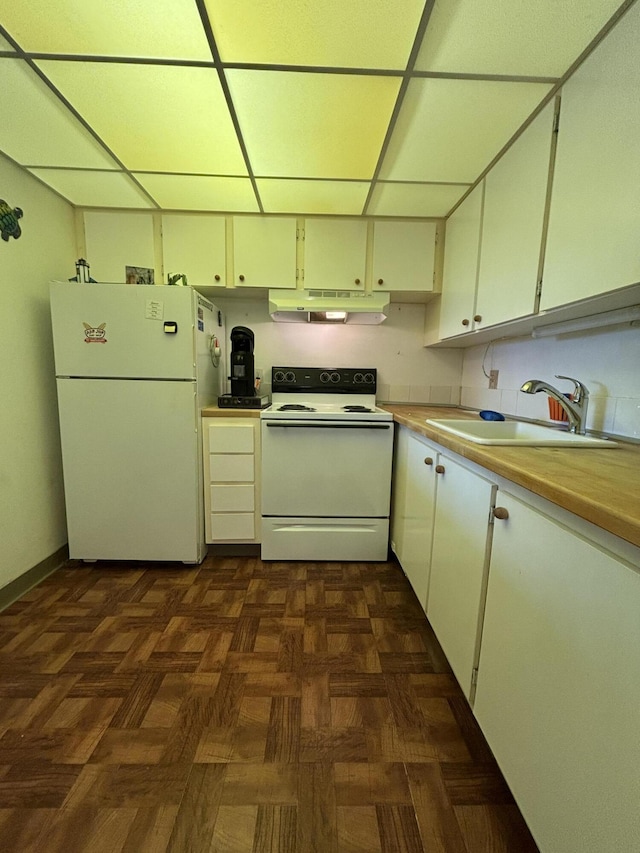 kitchen with dark parquet flooring, sink, a drop ceiling, white appliances, and white cabinets