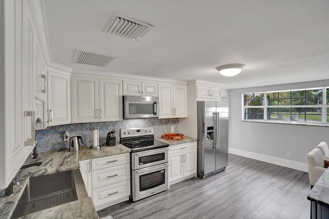 kitchen featuring light stone countertops, appliances with stainless steel finishes, backsplash, light hardwood / wood-style flooring, and white cabinets