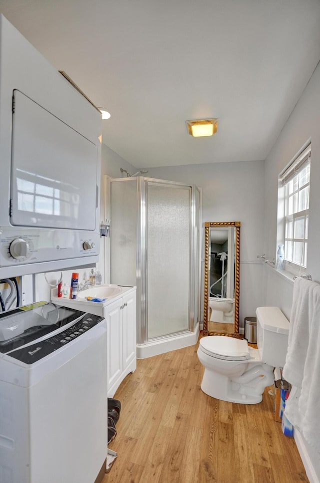 bathroom featuring vanity, a shower with door, wood-type flooring, toilet, and stacked washer / drying machine