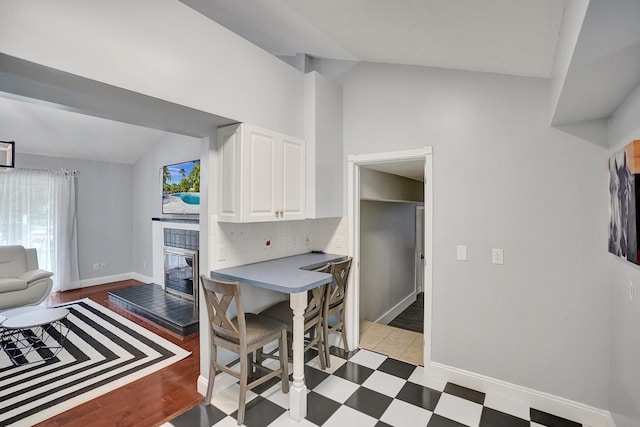 kitchen featuring lofted ceiling, light wood-type flooring, white cabinetry, and tasteful backsplash