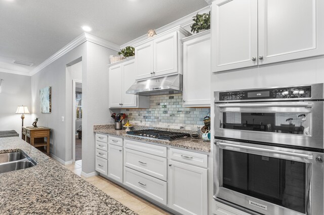 kitchen with under cabinet range hood, stainless steel appliances, white cabinetry, visible vents, and decorative backsplash