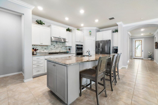 kitchen featuring arched walkways, under cabinet range hood, stainless steel appliances, visible vents, and backsplash