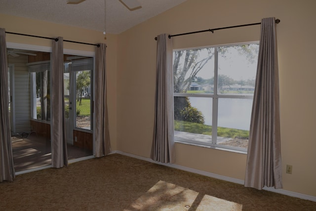 carpeted empty room with ceiling fan, a water view, lofted ceiling, and a textured ceiling