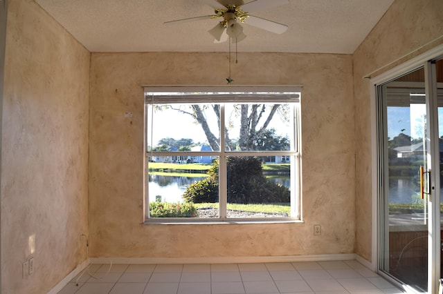 tiled empty room featuring ceiling fan, a water view, a healthy amount of sunlight, and a textured ceiling