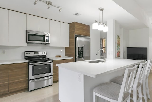 kitchen featuring sink, decorative light fixtures, light hardwood / wood-style floors, white cabinetry, and stainless steel appliances