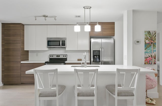 kitchen featuring pendant lighting, white cabinetry, a kitchen island with sink, and appliances with stainless steel finishes