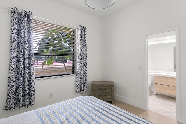 bedroom with connected bathroom, multiple windows, and light wood-type flooring