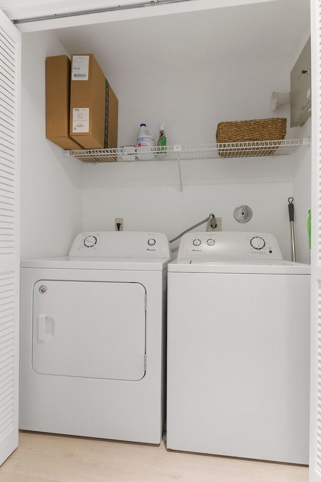 clothes washing area with washer and clothes dryer and light wood-type flooring