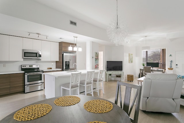 kitchen with an island with sink, decorative light fixtures, light hardwood / wood-style floors, stainless steel appliances, and a chandelier