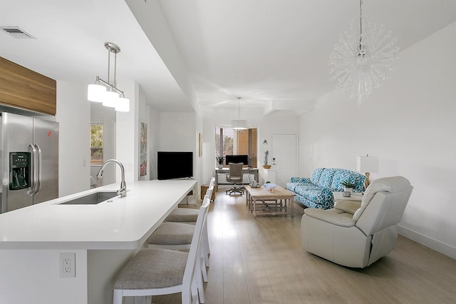 kitchen featuring stainless steel fridge, sink, pendant lighting, an inviting chandelier, and light hardwood / wood-style flooring