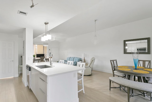 kitchen with appliances with stainless steel finishes, light wood-type flooring, sink, pendant lighting, and white cabinets