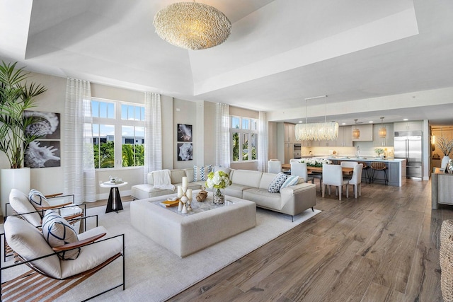 living room featuring a raised ceiling, a healthy amount of sunlight, a notable chandelier, and hardwood / wood-style flooring