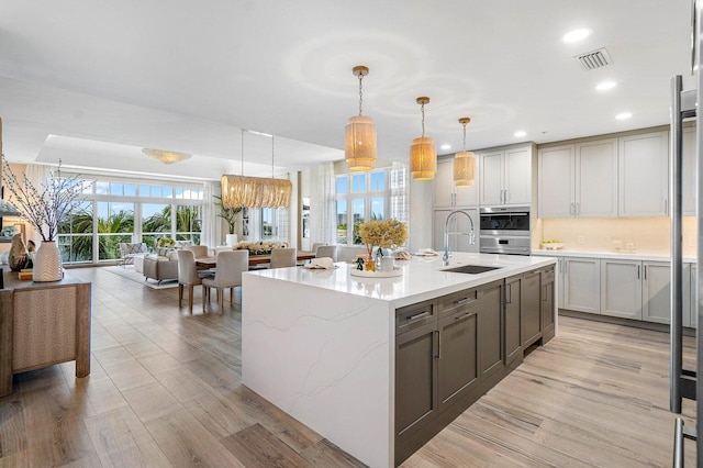 kitchen featuring a center island with sink, light hardwood / wood-style floors, light stone counters, and hanging light fixtures