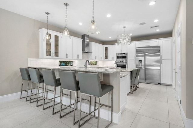 kitchen featuring wall chimney exhaust hood, kitchen peninsula, pendant lighting, white cabinets, and appliances with stainless steel finishes