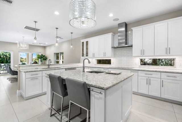 kitchen featuring a center island with sink, wall chimney exhaust hood, white cabinetry, and a chandelier