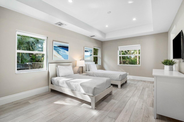 bedroom featuring a raised ceiling, light wood-type flooring, and multiple windows