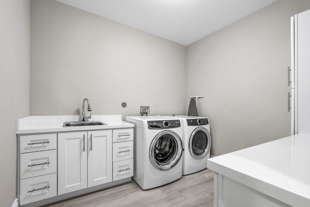 laundry area featuring washer and clothes dryer, sink, cabinets, and light wood-type flooring