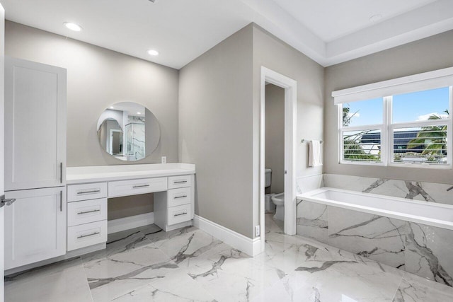 bathroom featuring tiled tub, vanity, and toilet